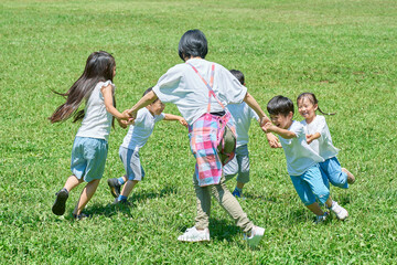 草原で輪になって遊ぶ子どもたちと女性