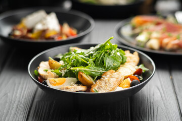 Chicken salad with arugula and crispy potatoes dressed with olive oil, garlic and lemon on black wooden background