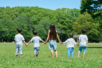 草原で手を繋いで並ぶ子どもたちの後ろ姿