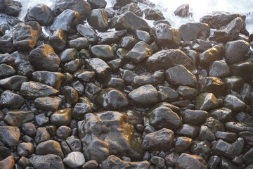 Ocean coast. The stones are saturated with surf waves in the rays of the morning sun. Beautiful background.