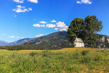 Fototapeta na wymiar The Sogn Mang chapel at Bonaduz, Grisons on the open field with big lush poplar trees in summer