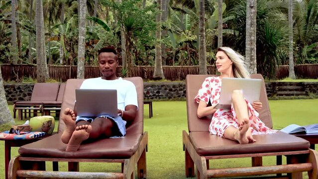 Mixed race couple working open air. Multicultural team high five. Multi ethnic people achieve goal. Interracial man lying sun chair. Palm tree park. Happy guy use laptop. Busy girl talk. Digital nomad