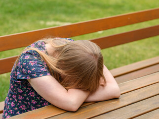 Smutna, płacząca młoda kobieta siedząca samotnie na ławce przy stole na świeżym powietrzu - obrazy, fototapety, plakaty