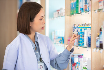 Professional pharmacist asian woman in uniform checking medicine stock inventory at shelf in drug store.