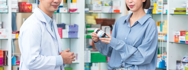 Asian man pharmacist advising and giving information to customer about medicine instructions in drugstore. Health care supplements concept.