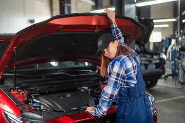Woman auto mechanic opens the hood of a car in a car service. 