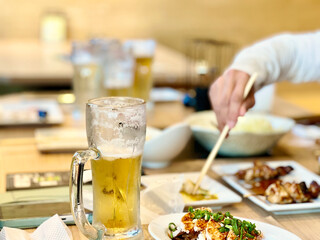 飲みかけのビールグラスと箸を伸ばす手元 © smile