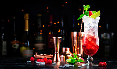 Raspberry lemonade cocktail or mocktail drink with raspberries, syrup, soda, lime, mint and ice, dark bar counter background, copy space