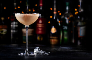 Rattlesnake alcoholic cocktail drink with coffee and cocoa liquor, irish cream, ground coffee and ice in glass, dark bar counter background, bar tools and bottles