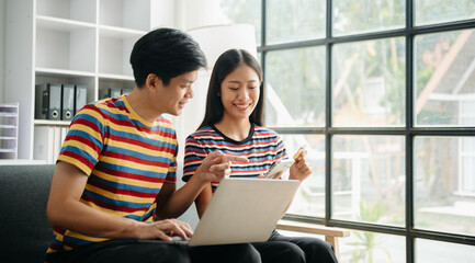 Two asian students learning together online with a laptop, tablet and tutor together in living room at home.