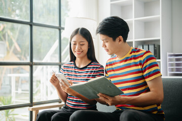 Fototapeta premium Two asian students learning together online with a laptop, tablet and tutor together in living room at home.