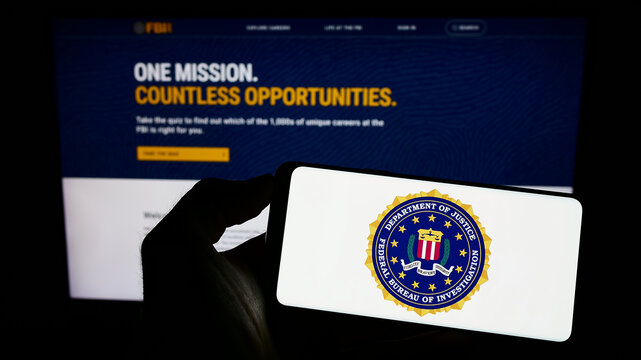 Stuttgart, Germany - 07-09-2023: Person holding smartphone with seal of US Federal Bureau of Investigation (FBI) on screen in front of website. Focus on phone display.