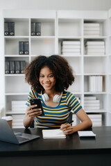  Beautiful African woman using laptop and tablet while sitting at her working place. Concentrated at work in home office