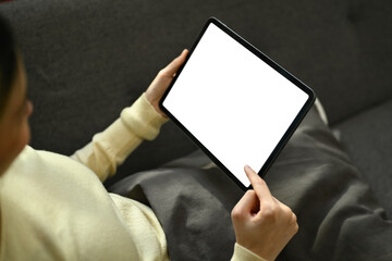 Young woman sitting on couch and using digital tablet. Empty screen for your advertising text message