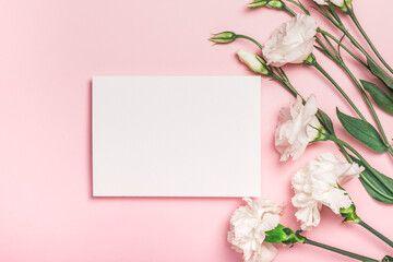 Delicate white eustoma flowers and white carnations and a blank card on a pink background. Postcard, invitation, congratulations
