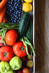 Wooden crate full of healthy seasonal fruit and vegetable. Top view, wooden background.