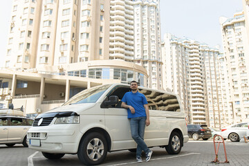 A man in a blue T-shirt leaned against a white car