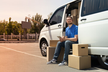 A courier with a tablet in his hands near a car with boxes