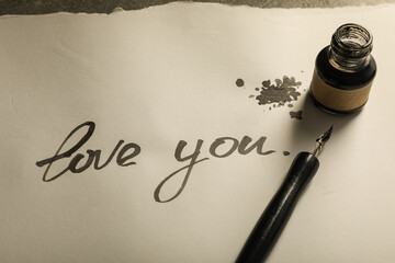 Ink bottle, pen and words Love you on paper on gray background, close up