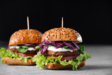 Two vegan burger with vegetables and sauce on dark background. Healthy food concept.