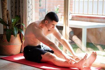 Young man concentrated shirtless stretching sitting on a mat