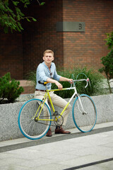 Businessman, office worker wearing stylish smart casual clothes, sitting on street, outside the office with bike. Urban background. Concept of business, active lifestyle, fashion, youth, ecology