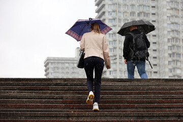 People with umbrellas climb the steps on a street. Rainy weather in summer or autumn city