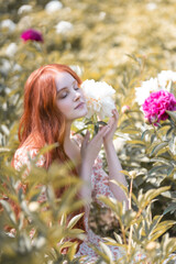 Red-haired girl with beautiful peonies in the summer garden
