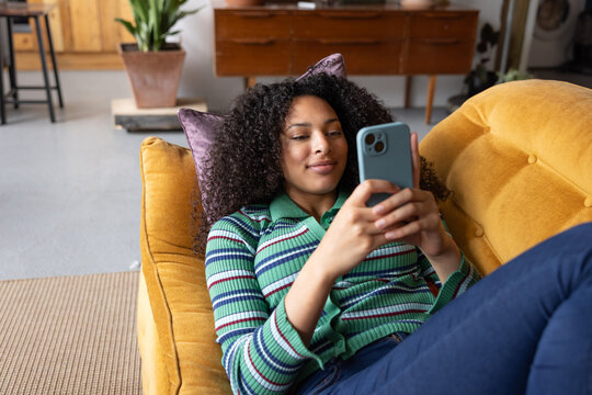 Young adult woman using smartphone lying on sofa 