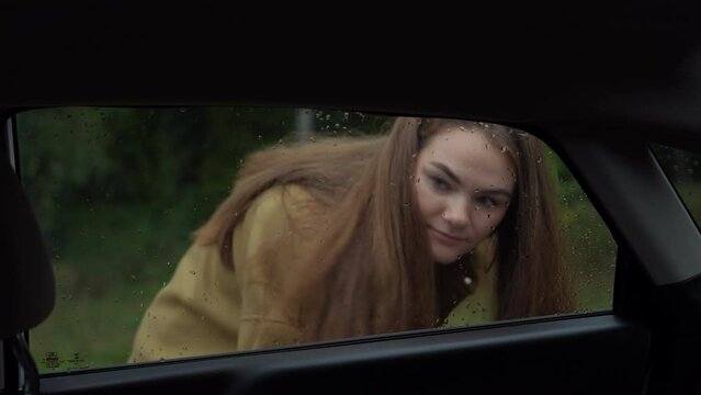 Shooting from car salon of young woman trying open door forgetting key. Anxious worried Caucasian lady having trouble on rainy overcast day with automobile