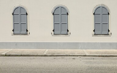 Closed gray arched shutters on a white facade. Concrete sidewalk and street in front. Background...