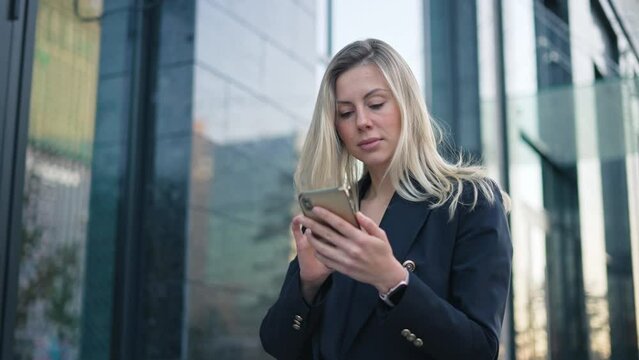 Serious confident 40s girl text message. Successful 30s business woman type job sms. Sexy boss lady use mobile cell phone chat close up. Pretty top manager walk. Blond hair person wear city work suit.