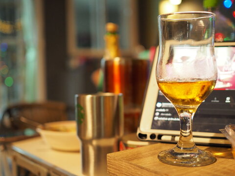 Almost half a mug of fresh beer placed on the wooden table.
This is a detailed photo of a glass,with a blurry background. 
Layer in the category of restaurant, bar and food or party.