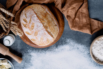 Fototapeta na wymiar Freshly baked wholemeal bread with rolling pin, milk, flour, ears of wheat on the basket, sprinkled with flour on a concrete table. Healthy food, vegan bread. top view.