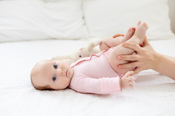 a small newborn baby girl lies on a white cotton bed at home, mother's hands stroke or do foot massage