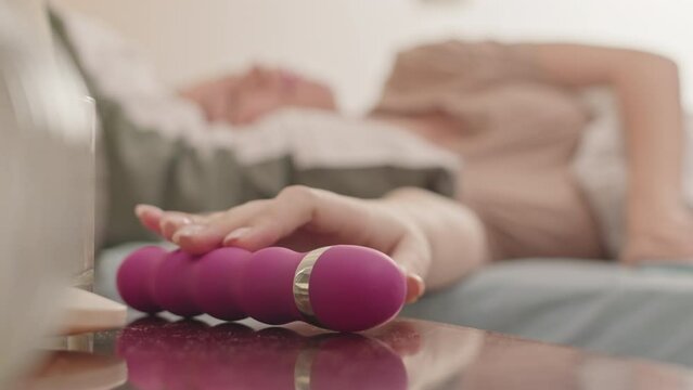 Young Caucasian woman taking pink vibrator from her nightstand while relaxing in bed alone in morning