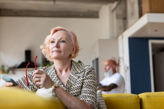Fashionable senior woman at home looking out of window thinking