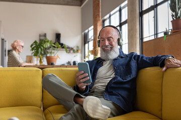 Trendy senior man at home using a smartphone with headphones to listen to music