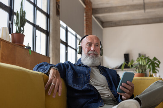 Fashionable senior man at home elearning using a smartphone with headphones
