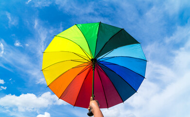 Hand holding colorful rainbow umbrella and blue sky background. LGBT, Pride Month, diversity, Sunprotect Concept..
