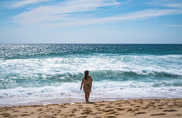 A girl is walking next to the calm ocean in Nazare, summertime, Portugal