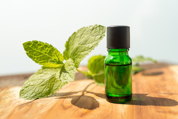 Green bottle of essential oils. natural cosmetics for skin care. A bottle and fresh mint on a wooden table. Taking care of health and beauty.