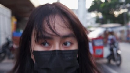 Close-up dramatic shot of a distressed Asian, black-haired woman in a face mask walking through the streets of Manila, Philippines. - Powered by Adobe
