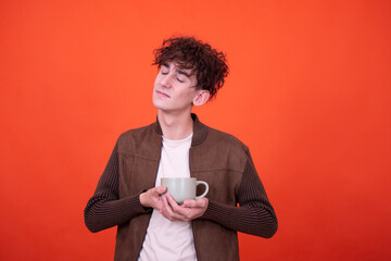Funny guy is holding a mug with coffee and posing on an orange background.