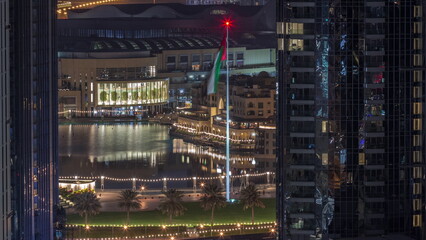 Aerial view of Dubai Fountain in downtown with palms in park next to shopping mall and souq night to day timelapse, UAE