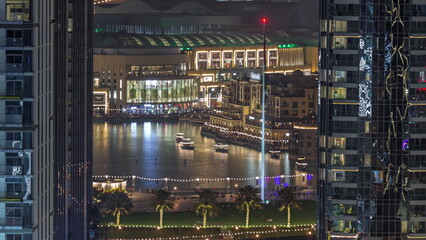 Aerial view of Dubai Fountain in downtown with palms in park next to shopping mall and souq night timelapse, UAE