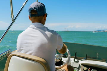 Bach view of middle-aged man driving luxury motor yacht. Captain at the helm of motor boat.