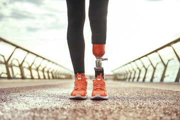 Cropped photo of disabled woman with prosthetic leg in sportswear standing on the bridge