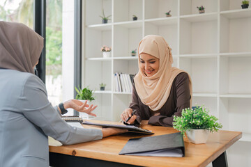 Young muslim female business worker discussing with friends sitting together, working with tablet and financial documents at desk