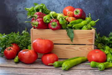 Various vegetables on a wooden table. Tomato, Green Pepper, Red Pepper, Parsley, Carrot.